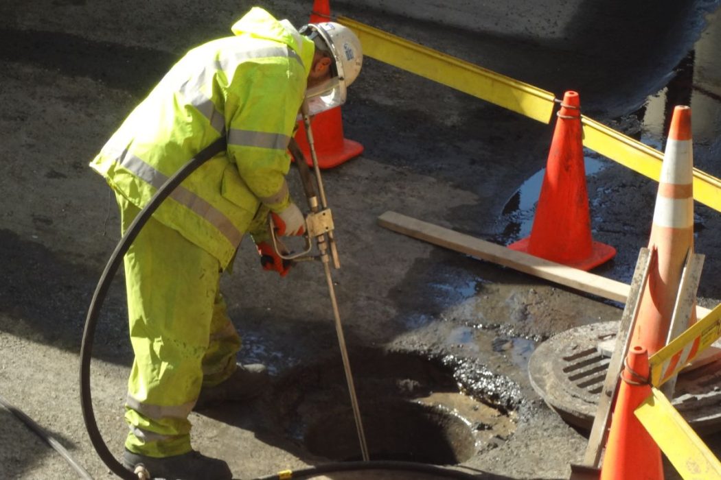 Worker cleaning manhole with hose